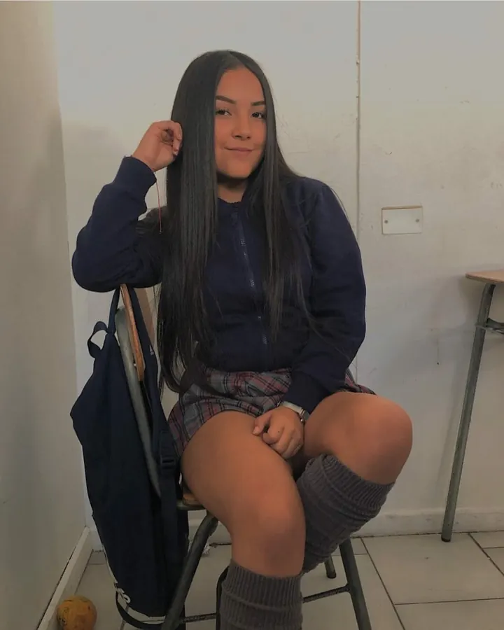 Jeune femme aux cheveux bruns foncés en haut noir, posant de face dans une pièce, regardant vers la caméra.