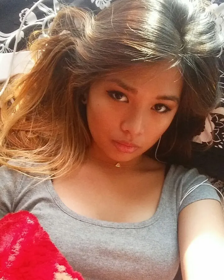 Femme aux cheveux bruns en haut noir, souriante, dans une chambre avec un lit