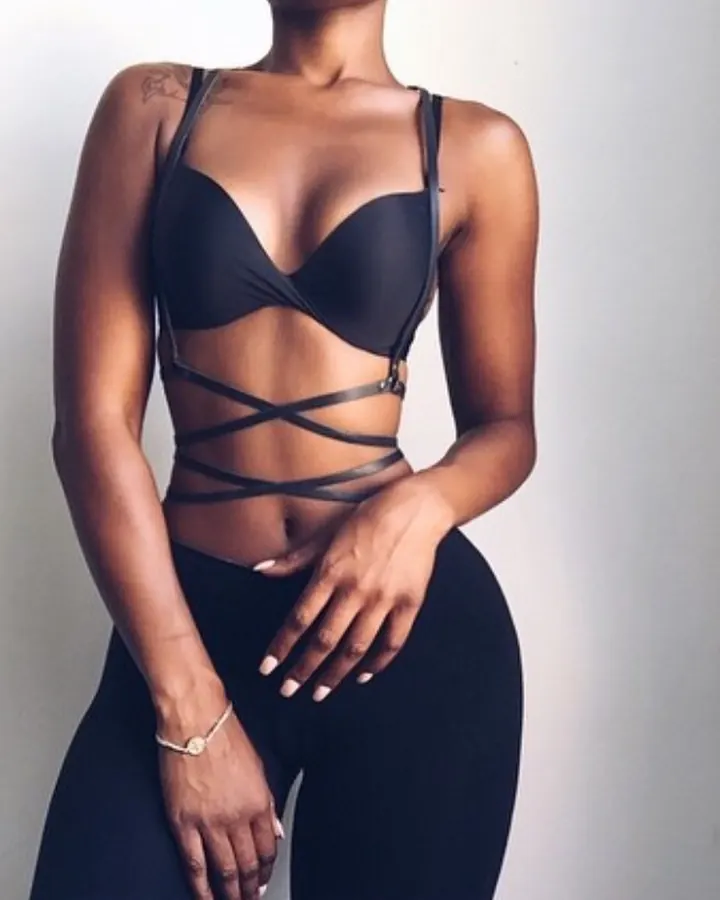 Femme en lingerie noire, tenant son ventre, debout contre un mur blanc