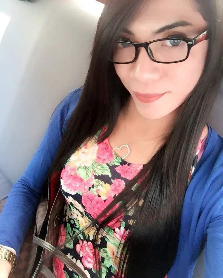 Femme aux cheveux noirs, portant des lunettes, une veste bleue et un haut à motifs floraux, assise dans une voiture.
