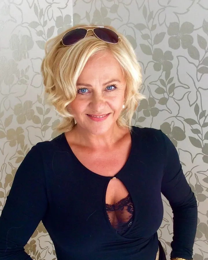 Femme aux cheveux blonds, portant un haut noir et un short noir, prenant un selfie dans une chambre.