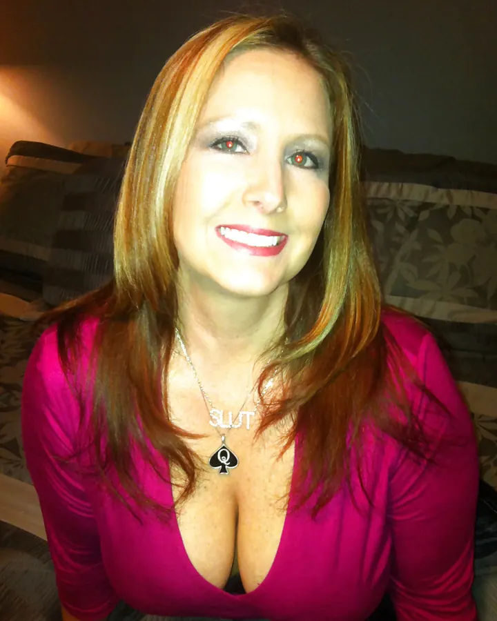Femme blonde en rose vif, sourire large, collier « SLUT »
