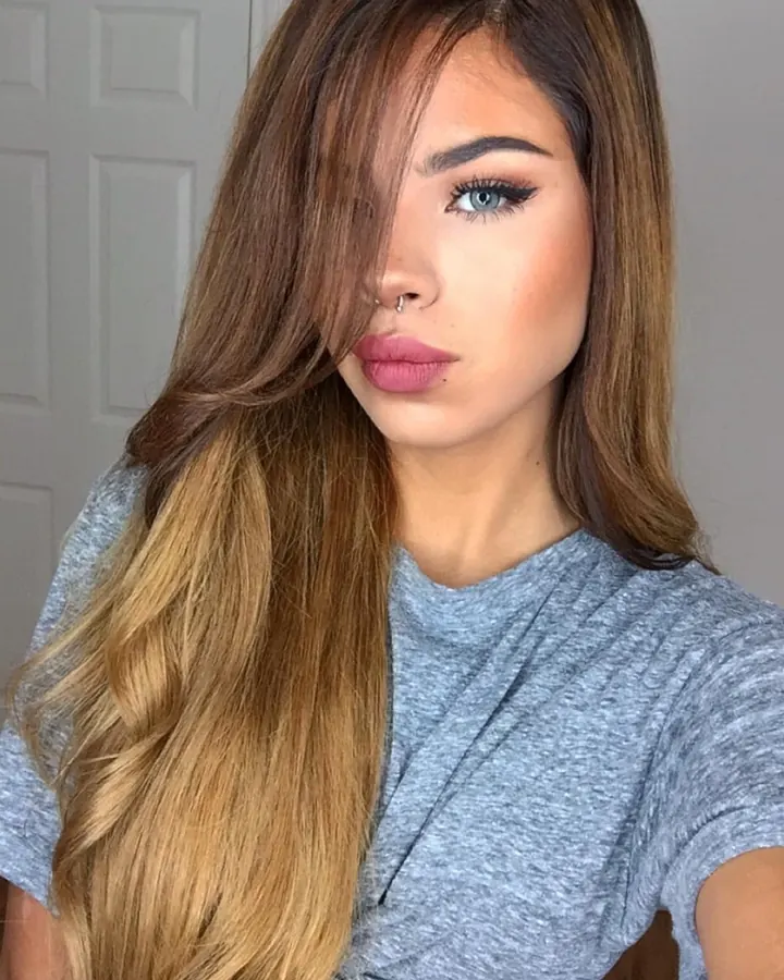 Femme aux cheveux blonds mi-longs, yeux bleus, maquillage soigné, portant un t-shirt gris, regard direct vers l'appareil.