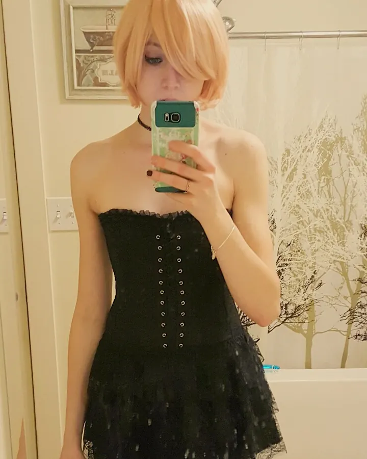 Jeune femme blonde prenant un selfie devant un miroir, portant un haut rose et un short noir avec bordure rose, tenant un téléphone à motifs.