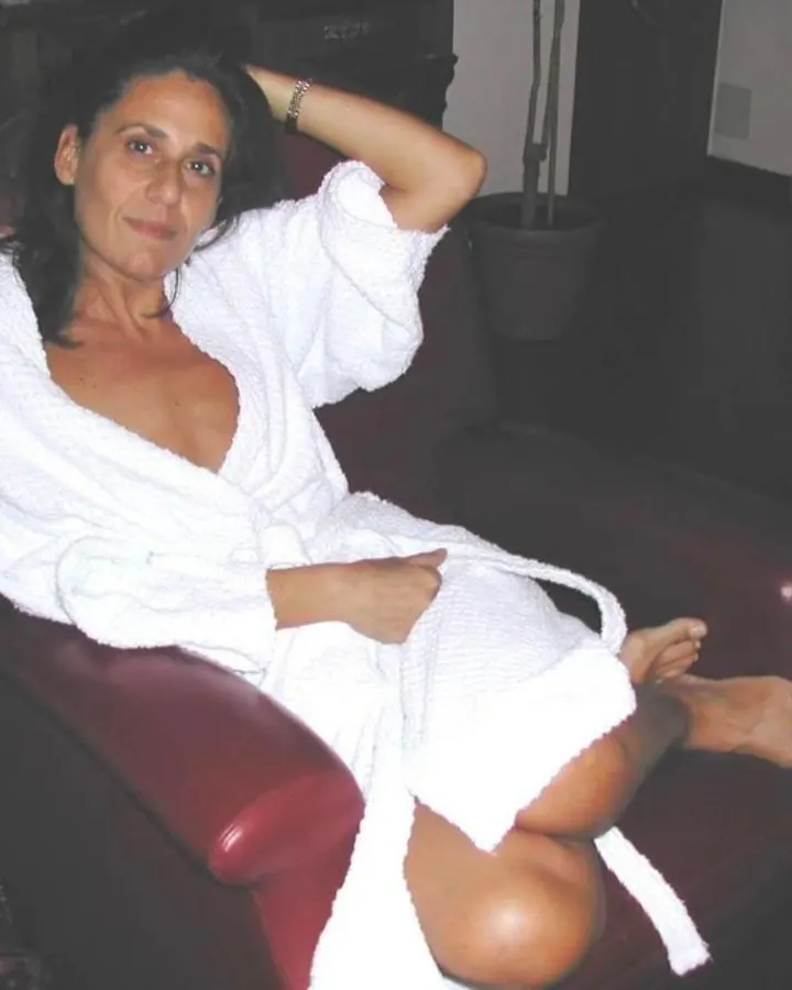 Femme aux cheveux bruns longs, vue de profil, portant un haut de sport rose et noir avec découpes, et un legging rose vif, sur une terrasse.