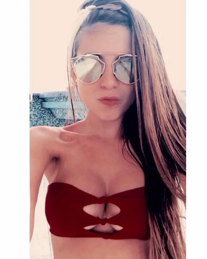 Femme aux cheveux blonds, vue de profil, portant un haut de sport rose et noir avec découpes, et un legging rose vif, sur une terrasse.