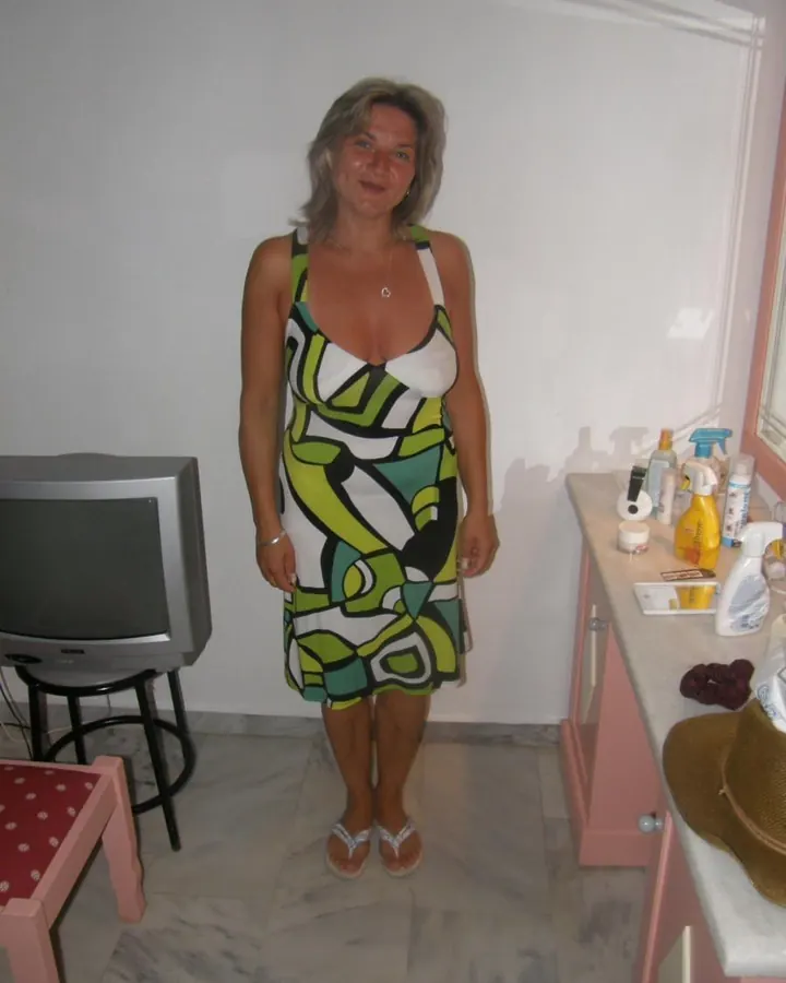 Femme aux cheveux gris, portant une robe à motifs géométriques verts, blancs et noirs, debout dans une pièce.