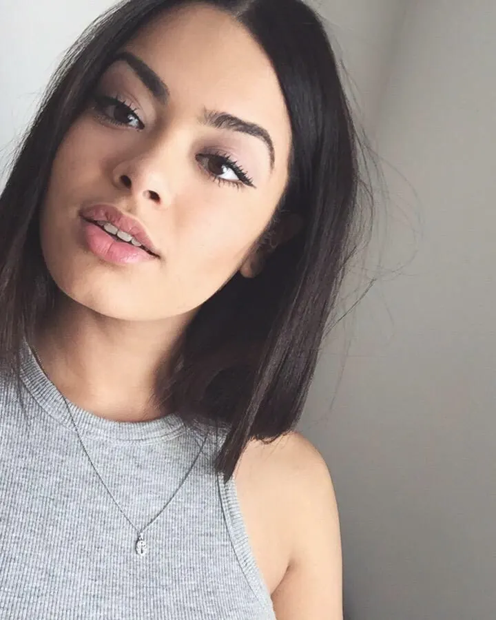 Jeune femme latine aux cheveux noirs mi-longs, portant un débardeur gris clair, regardant l'appareil avec un léger sourire.