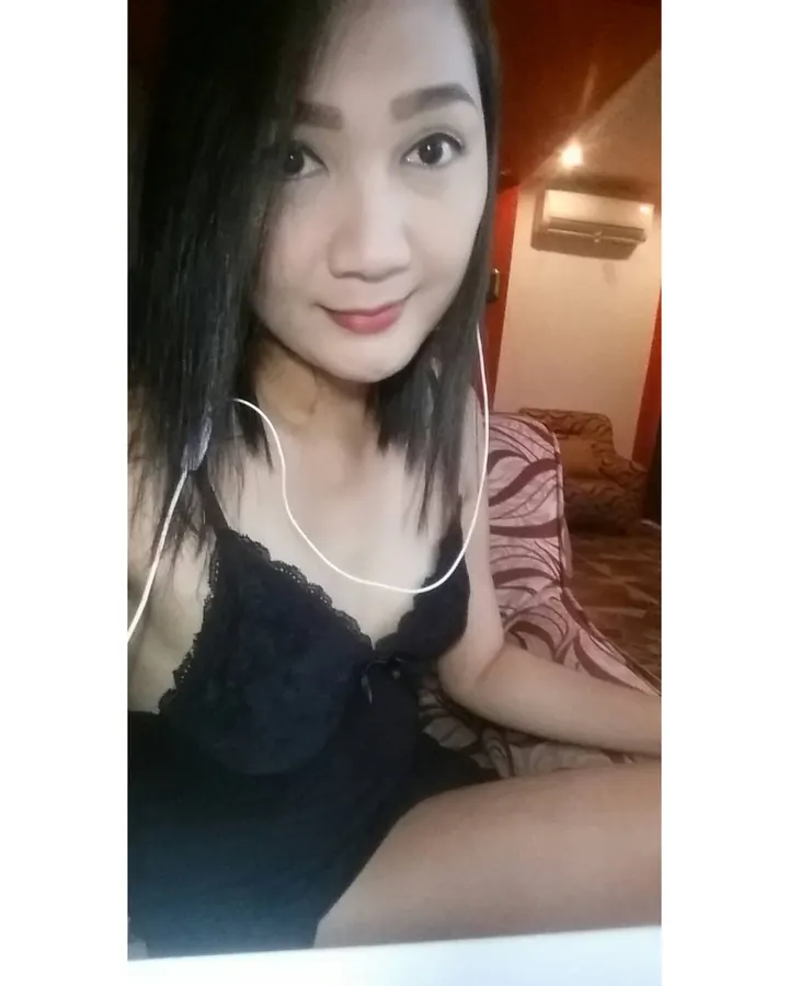 Jeune femme asiatique aux cheveux noirs, portant un haut noir à dentelle, souriant légèrement devant un miroir.