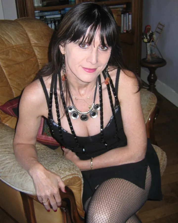 Femme aux cheveux bruns, en haut noir, assise sur un canapé en cuir, regardant l'appareil photo.