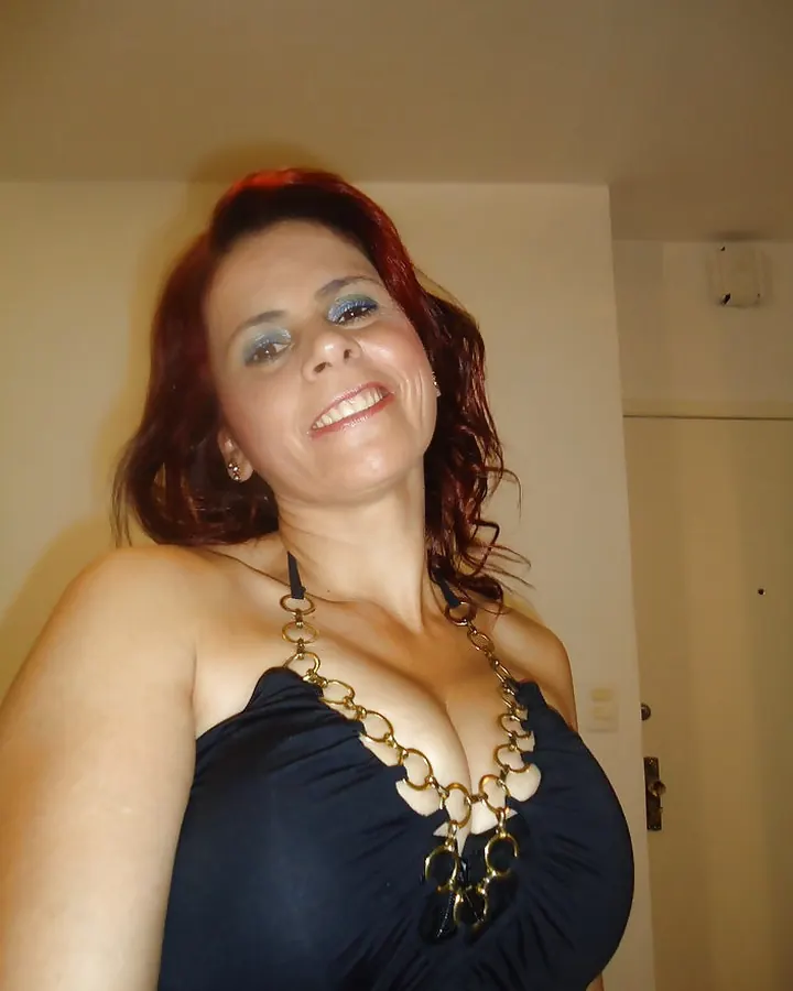 Femme blonde aux cheveux longs, portant un haut noir, souriant à la caméra, avec un piercing au nez et des yeux sombres.