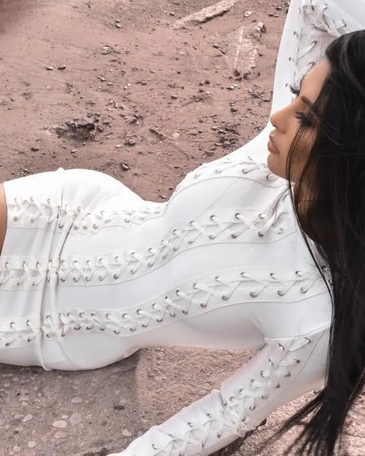Femme aux cheveux noirs allongée sur le sol en robe blanche à lacets, regard vers le côté