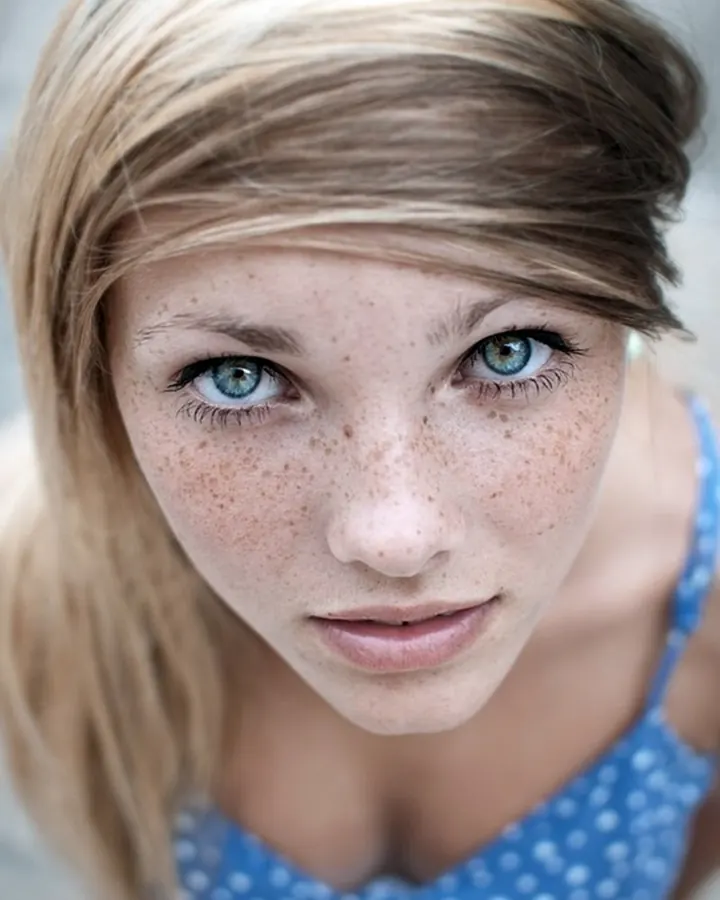 Jeune femme aux yeux bleus et taches de rousseur, regard direct vers l'objectif, haut bleu à pois