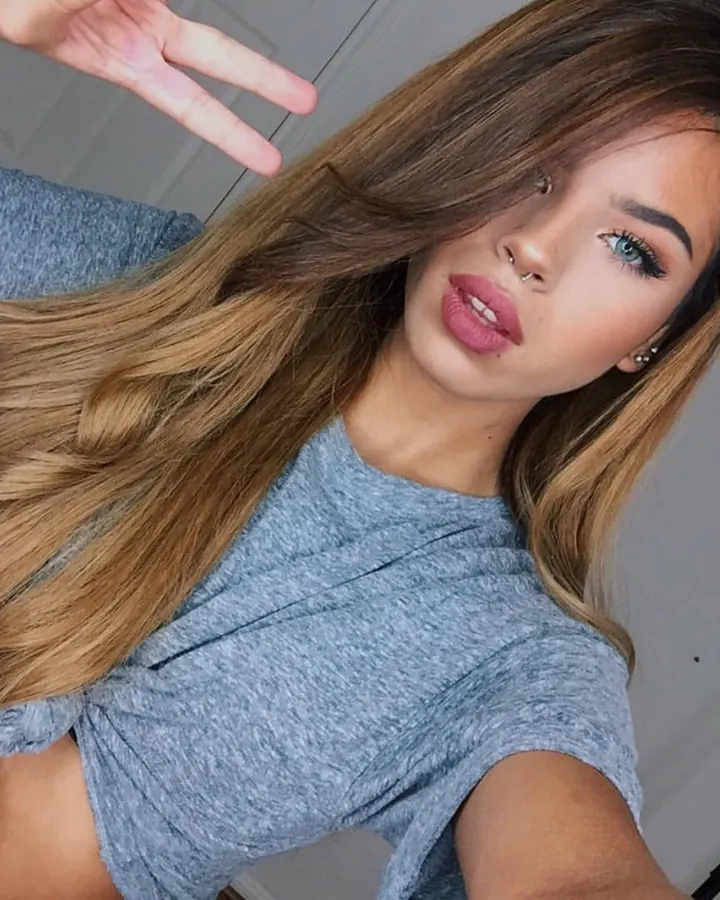 Jeune femme aux longs cheveux blonds et bruns, piercing au nez, regard direct, sweat gris noué