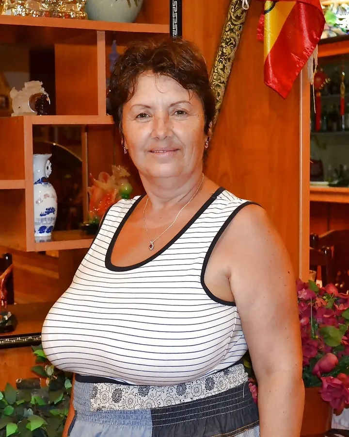 Femme aux cheveux bruns courts, en haut rayé blanc et noir, souriant devant une étagère avec des objets décoratifs.