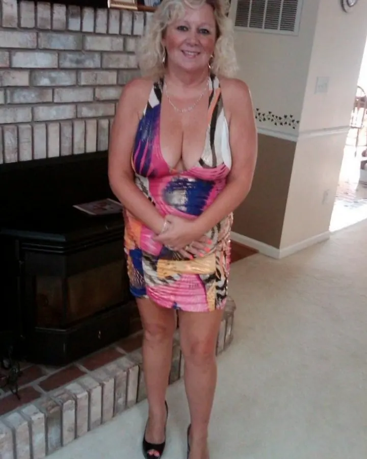 Femme en robe multicolore, debout près d'une cheminée, sourire, cheveux blonds bouclés