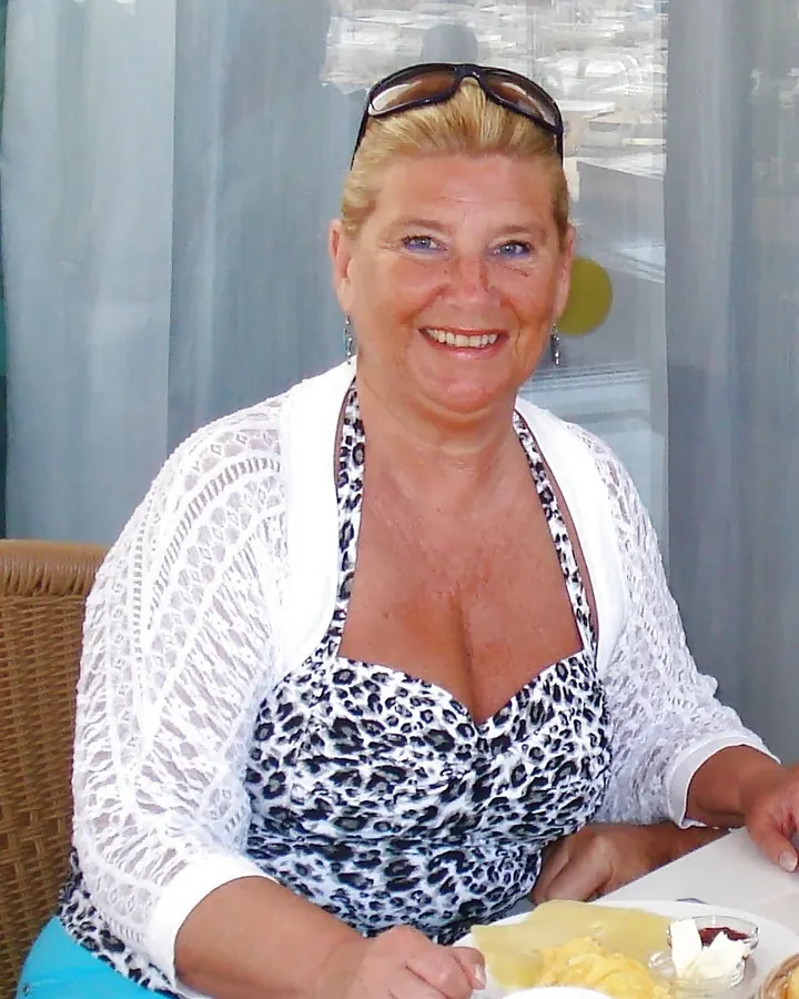Femme blonde en robe léopard, assise à une table avec des lunettes de soleil sur la tête