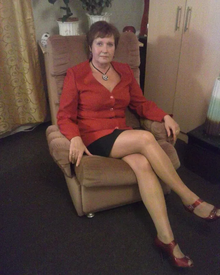 Femme aux cheveux châtains en robe rouge, assise dans un fauteuil beige