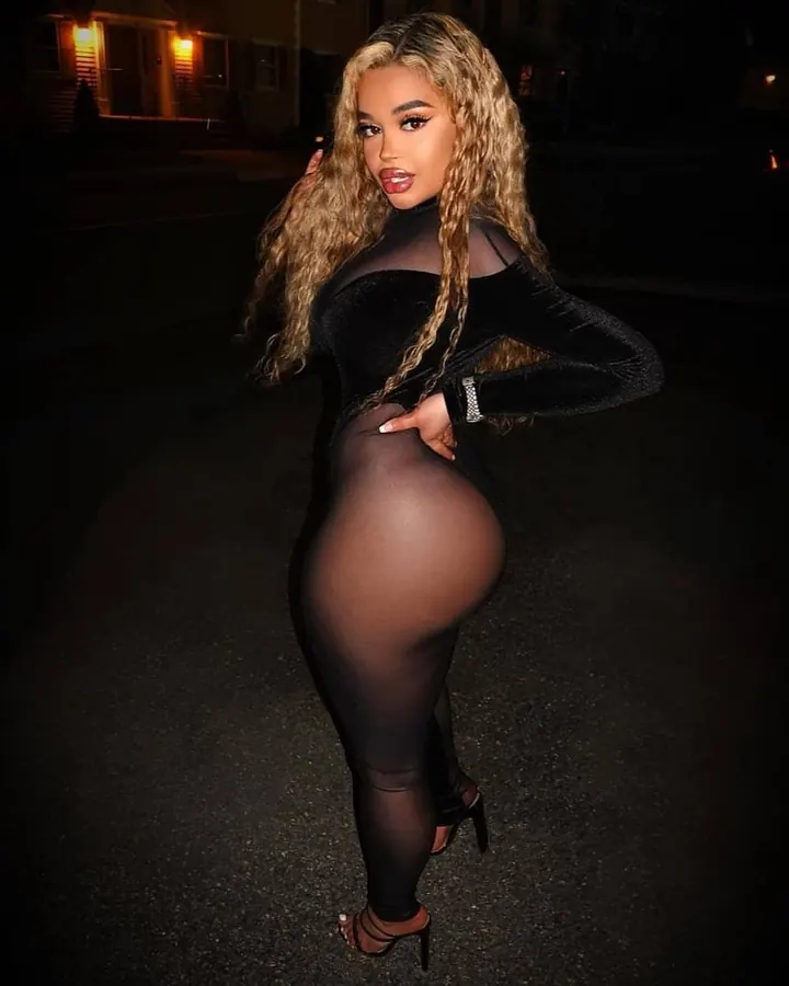 Femme africaine aux cheveux longs, en body noir transparent et collants, posant de profil dans la nuit.