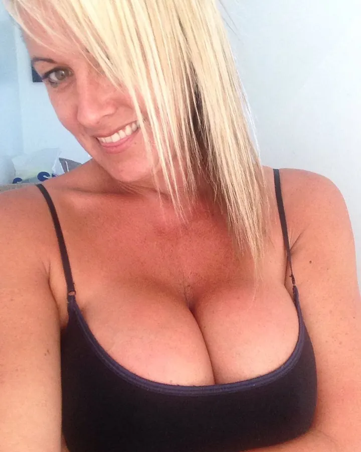 Femme blonde, en haut noir, souriant, regardant vers le côté, dans un intérieur clair.
