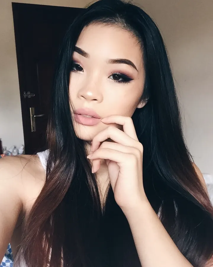 Jeune femme asiatique aux cheveux bruns, en haut jaune, regardant l'appareil avec un air pensif.