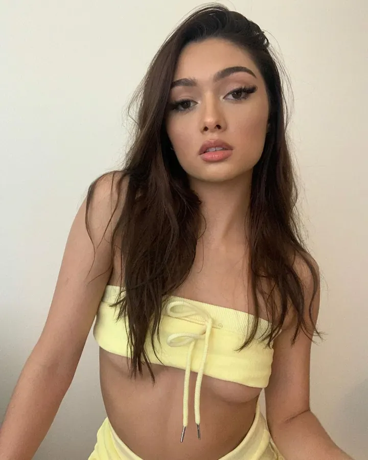 Jeune femme asiatique aux cheveux châtains, en haut jaune, regardant l'appareil avec un air pensif.