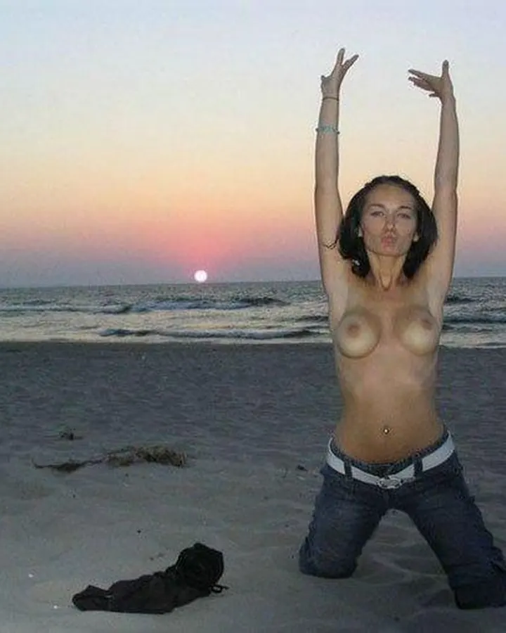 Femme nue sur une plage au coucher du soleil, genoux fléchis, bras levés