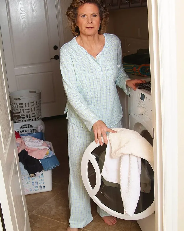 Femme en pyjama bleu clair dans une buanderie, tenant une serviette près d'une machine à laver