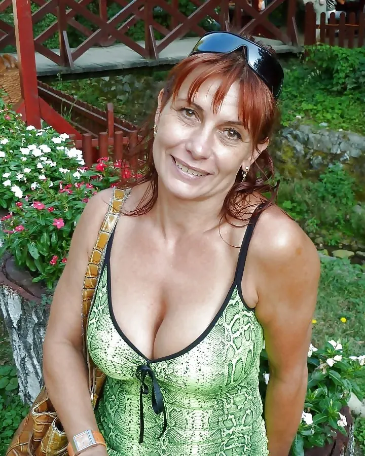 Femme aux cheveux roux souriante, en robe verte à imprimé serpent, dans un jardin verdoyant.