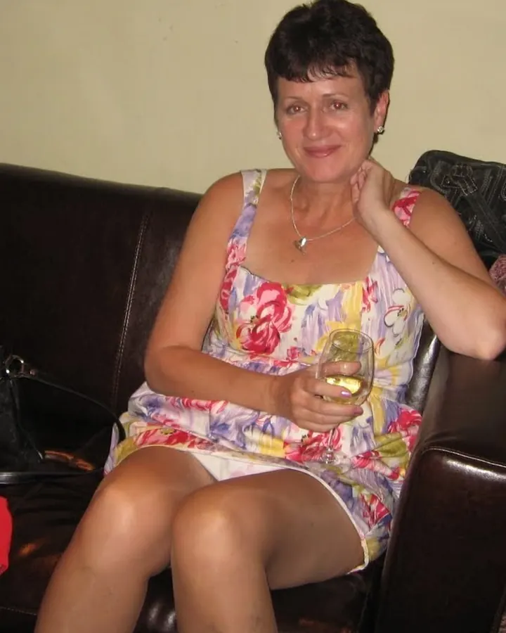 Femme assise sur un canapé, portant une robe fleurie, tenant un verre de vin blanc.