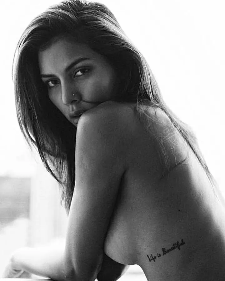 Femme en noir et blanc, torse nu, tatouage sur l'épaule, regardant vers le côté.