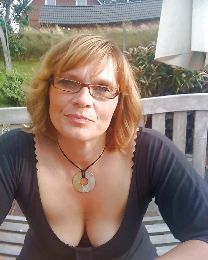 Femme aux cheveux blonds courts, portant des lunettes et un haut noir, souriant légèrement.