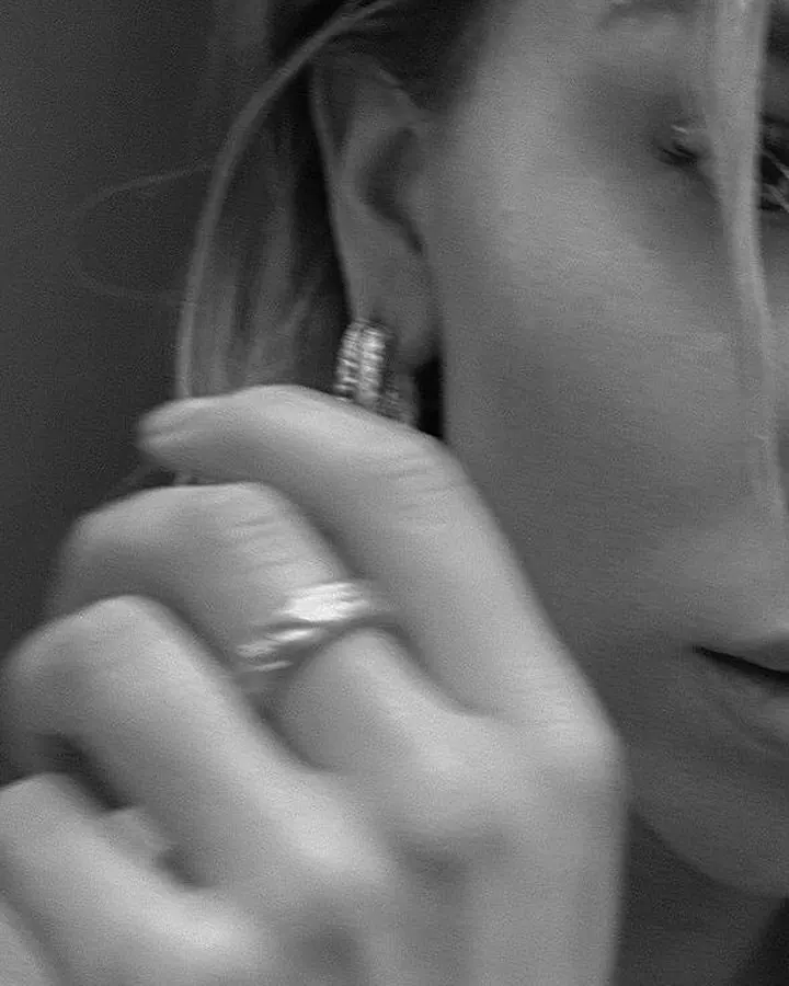 Plan rapproché d'une femme aux cheveux clairs, doigt touchant l'oreille, regard intense en noir et blanc