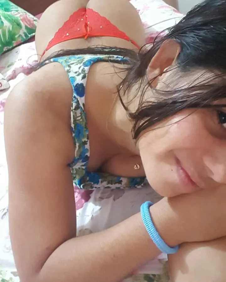 Femme aux cheveux foncés en sous-vêtements colorés, allongée sur un lit floral, regardant vers l'appareil