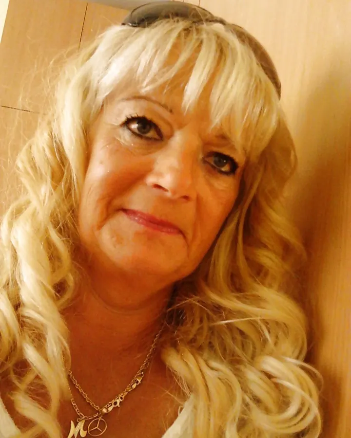 Femme blonde en haut noir, tenant ses seins, regardant l'appareil dans une chambre