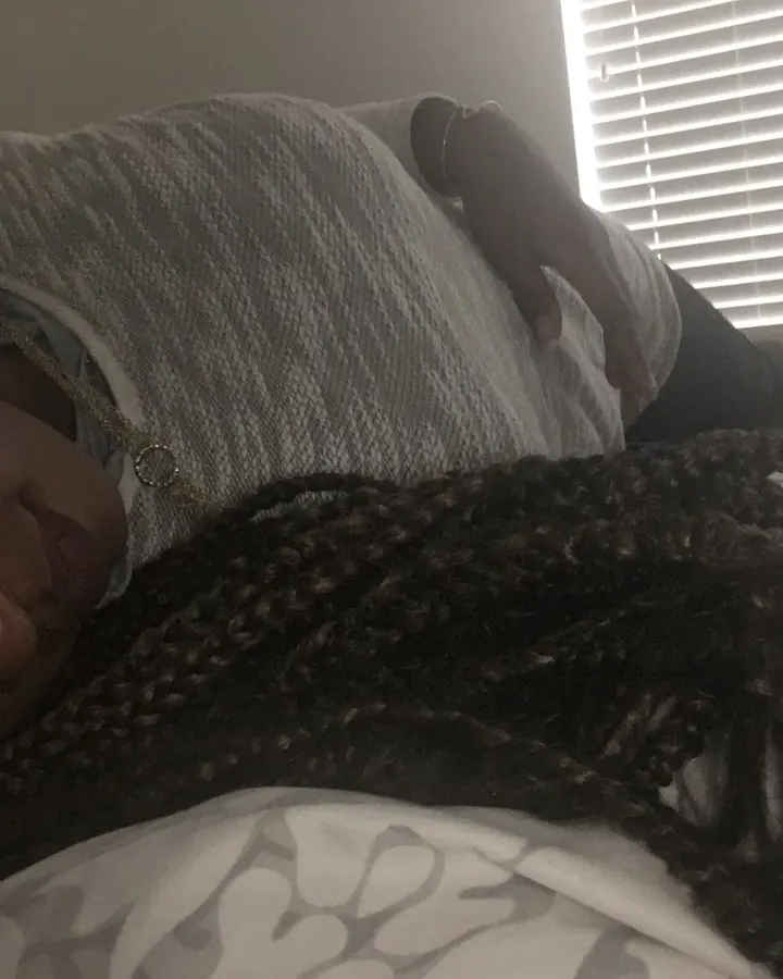 Femme en pyjama gris, allongée sur un lit, regardant l'objectif, cheveux tressés.