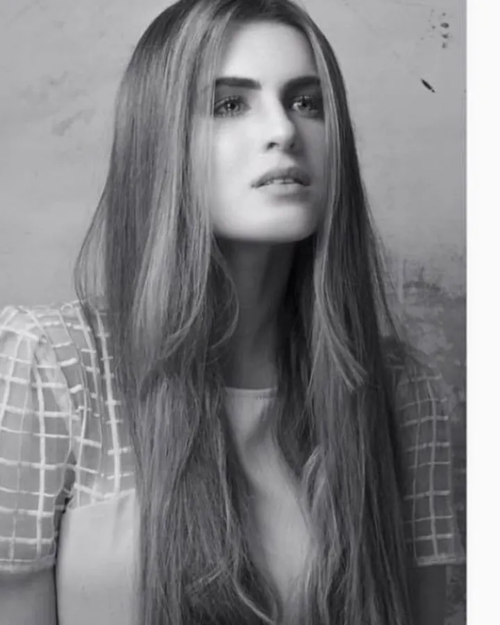 Portrait en noir et blanc d'une jeune femme aux longs cheveux, regardant vers le côté, vêtue d'un haut à carreaux.