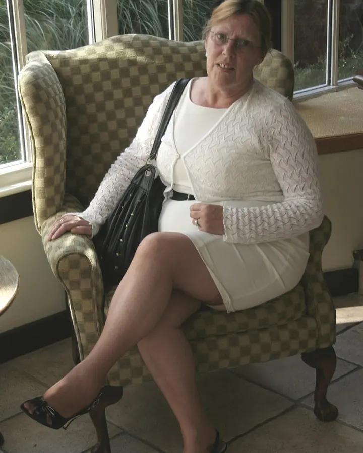 Femme blonde en tenue de soirée, posant sur un banc en extérieur, avec un fond de ciel crépusculaire et de mer.