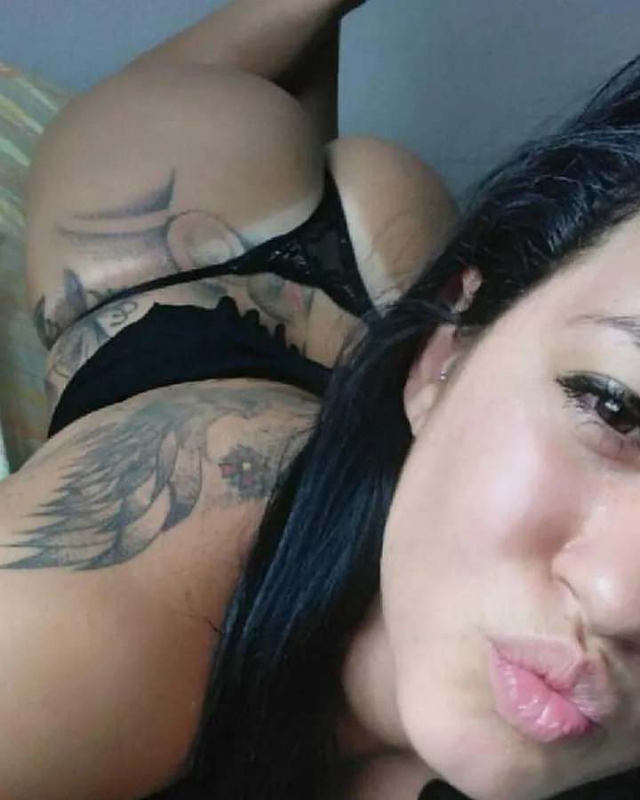Femme asiatique de 25 ans en intérieur, sous-vêtement noir, tatouages visibles sur bras, cheveux noirs longs, regard direct, pose allongée sur lit.