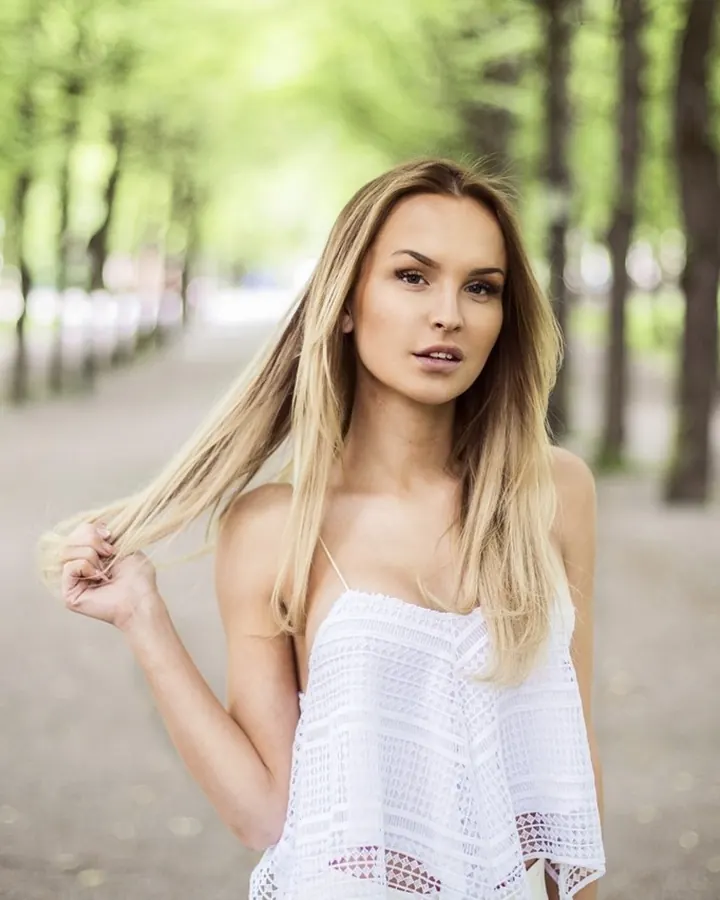 Femme blonde, en maillot de bain rose, souriante, les bras levés, dans une chambre