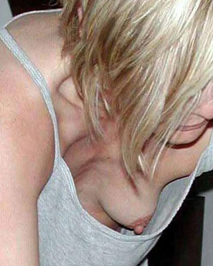 Jeune femme blonde en haut gris, penchée en avant, visage caché par ses cheveux.
