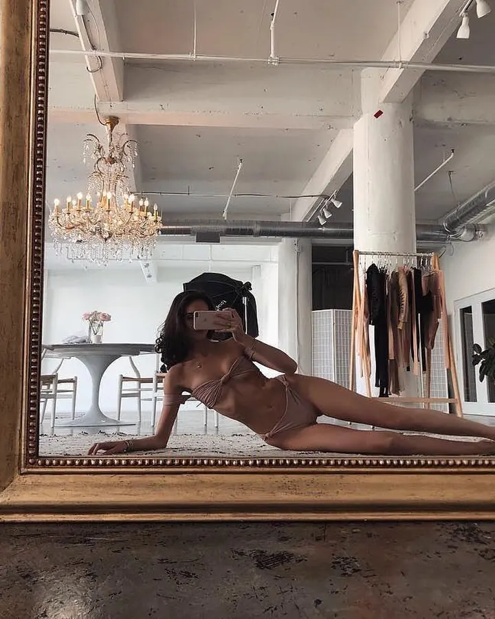Femme en lingerie bleue posant sur un canapé blanc dans une pièce lumineuse