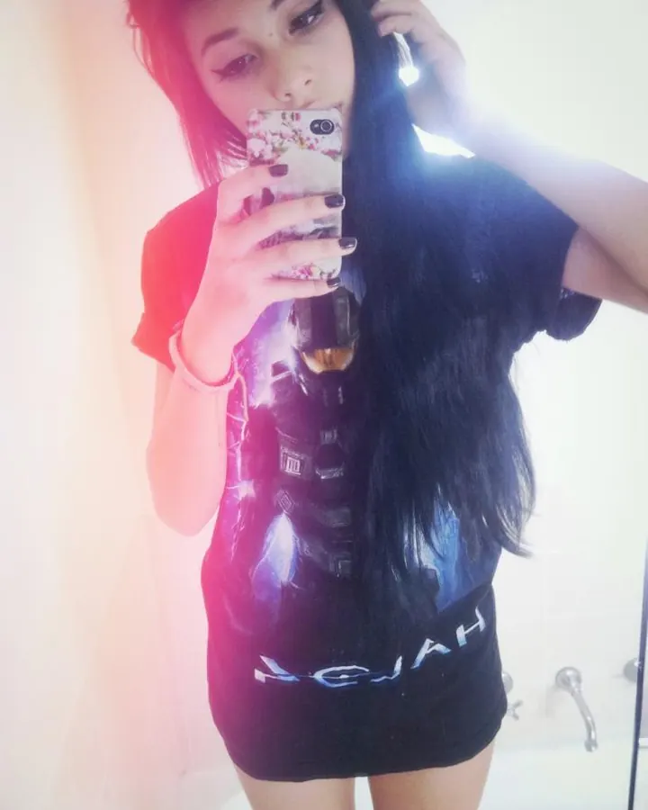 Jeune femme aux cheveux noirs, en t-shirt noir, prenant un selfie dans une salle de bain, lumière vive