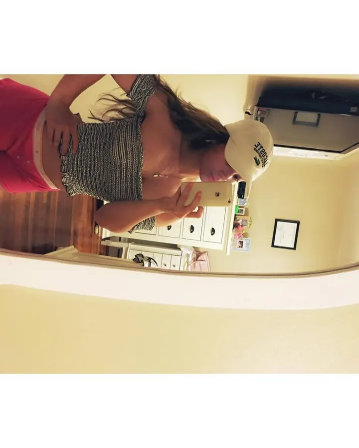 Femme blonde portant un haut rayé et un short rose, prenant un selfie dans un miroir.