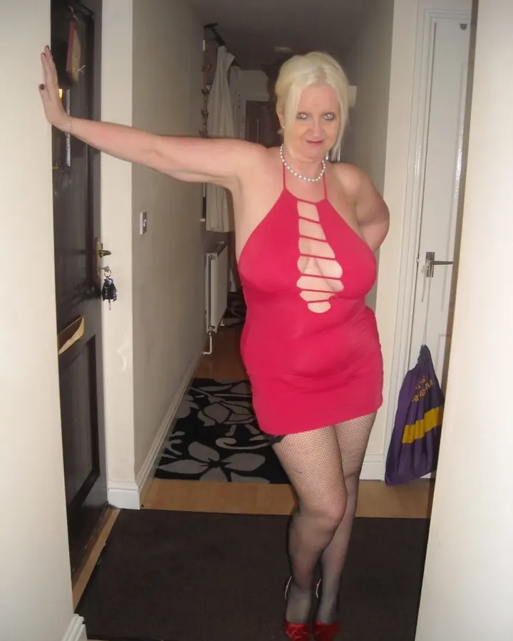 Femme en robe rouge fendue, collant résille, talons rouges, dans un couloir.